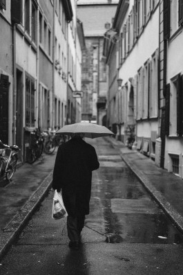 Mann mit Regenschirm läuft eine Gasse entlang 